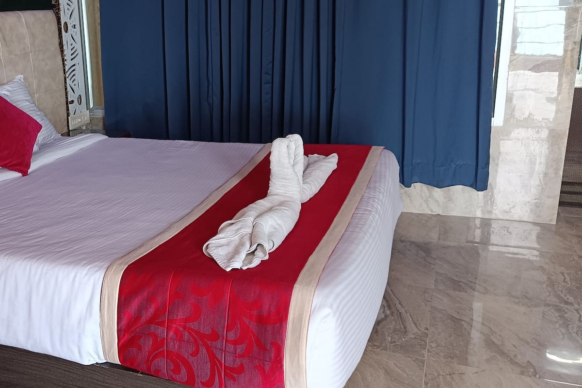 A neatly made bed with white and red bedding, a wooden nightstand, and a blue curtain in the background.