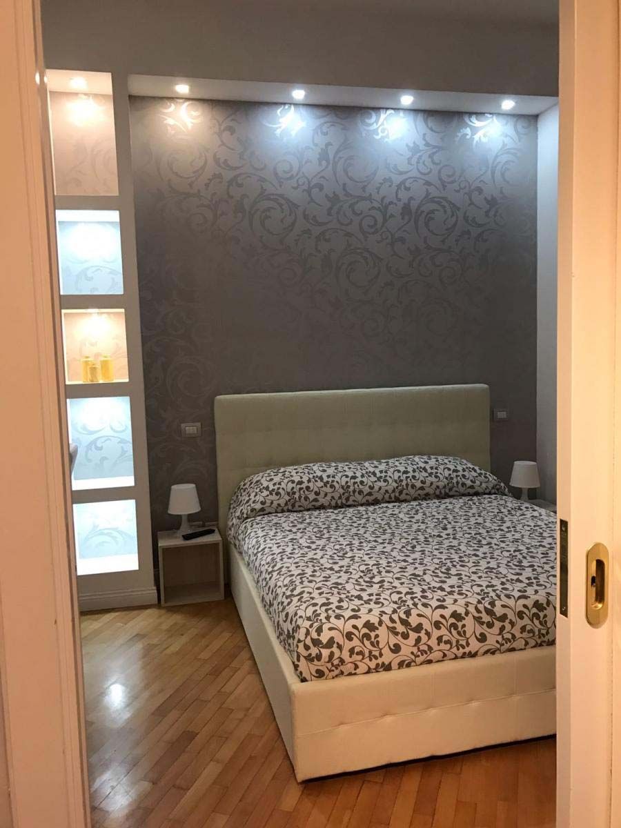 A bedroom with a bed, nightstands, and a wall with patterned wallpaper.