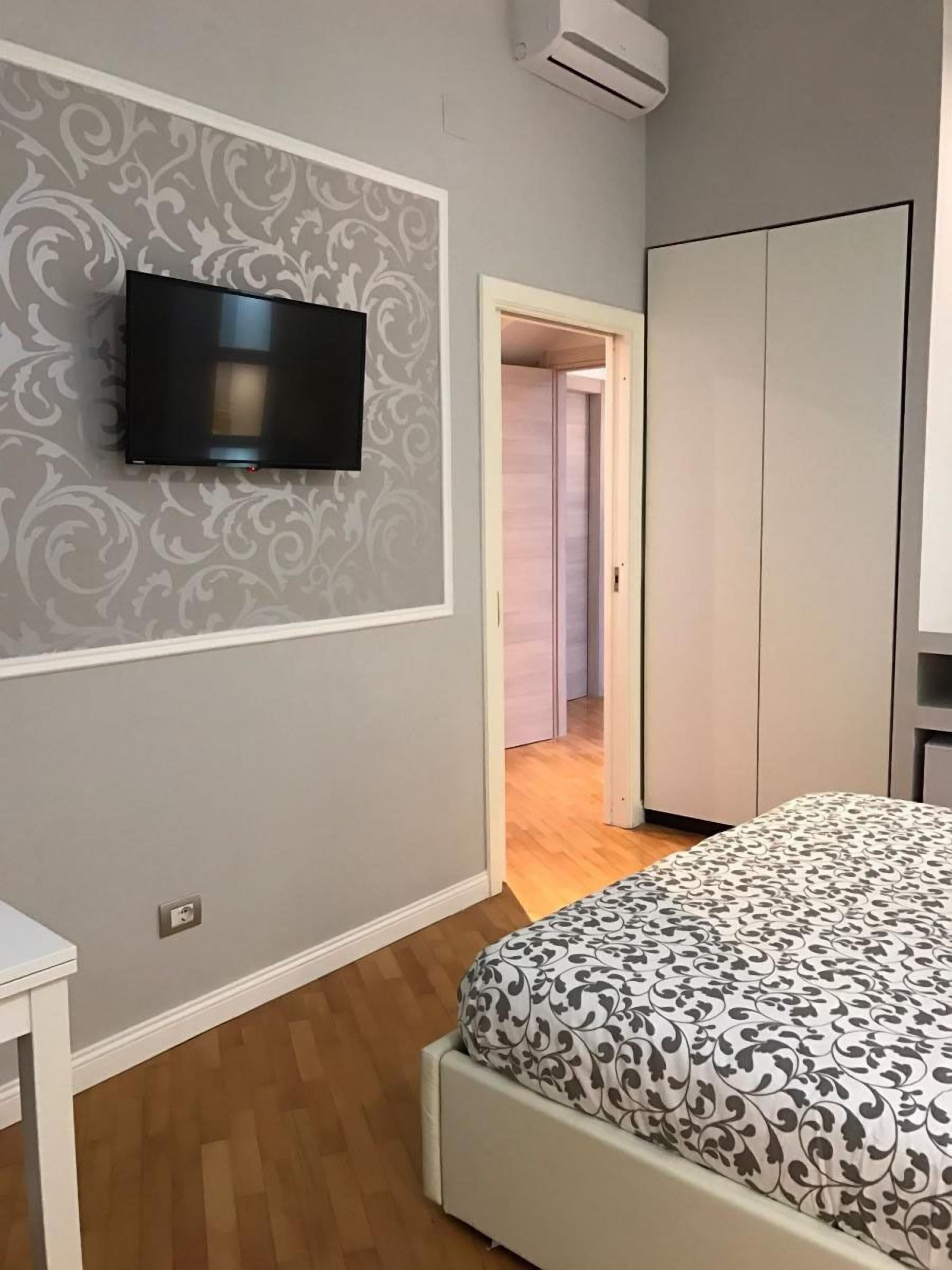 Une chambre à coucher comprenant un lit, une armoire, un téléviseur fixé au mur et une porte donnant sur une autre pièce.