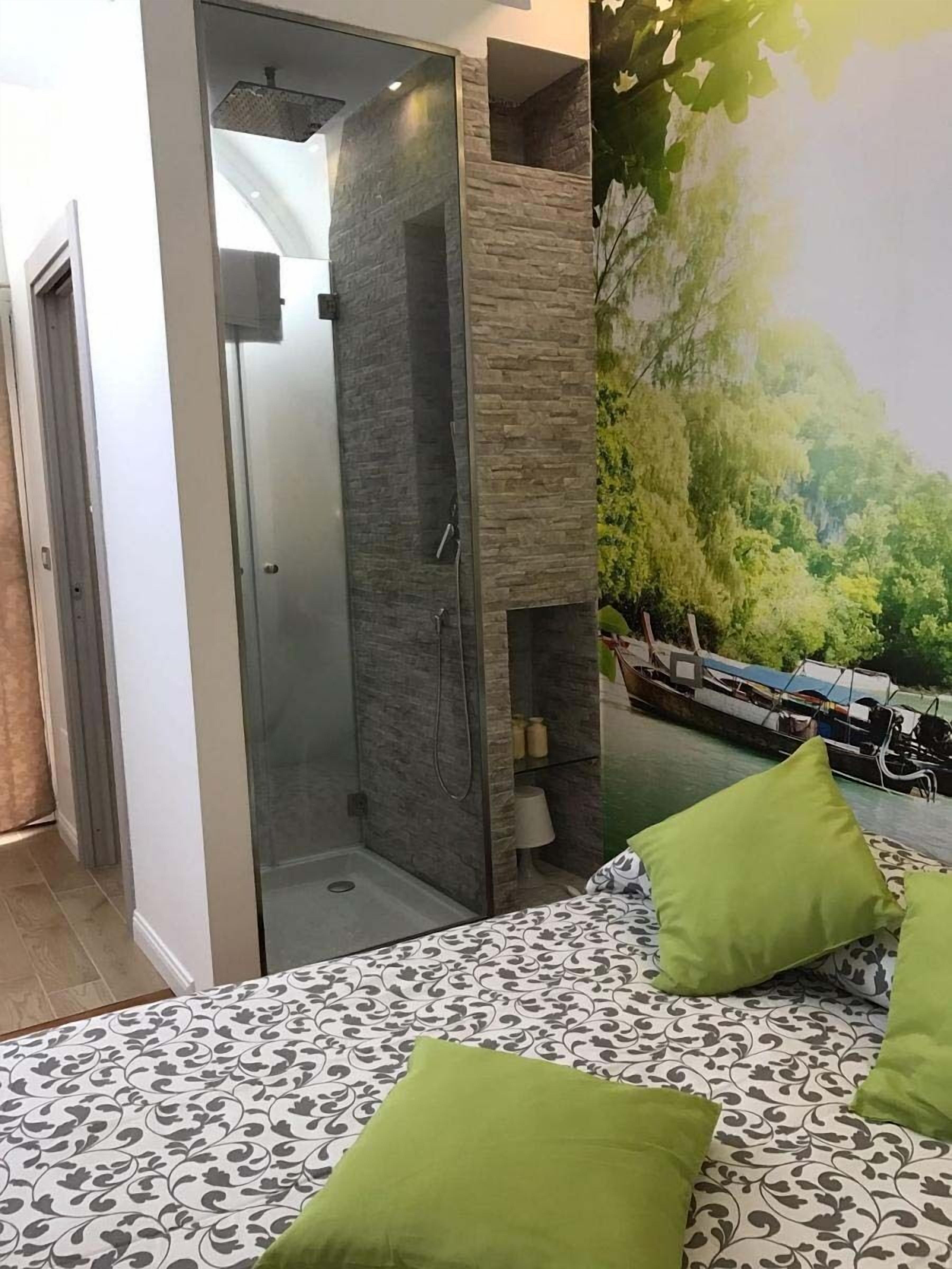Un dormitorio con cama, almohadas verdes, cabina de ducha y un mural que representa un paisaje fluvial.