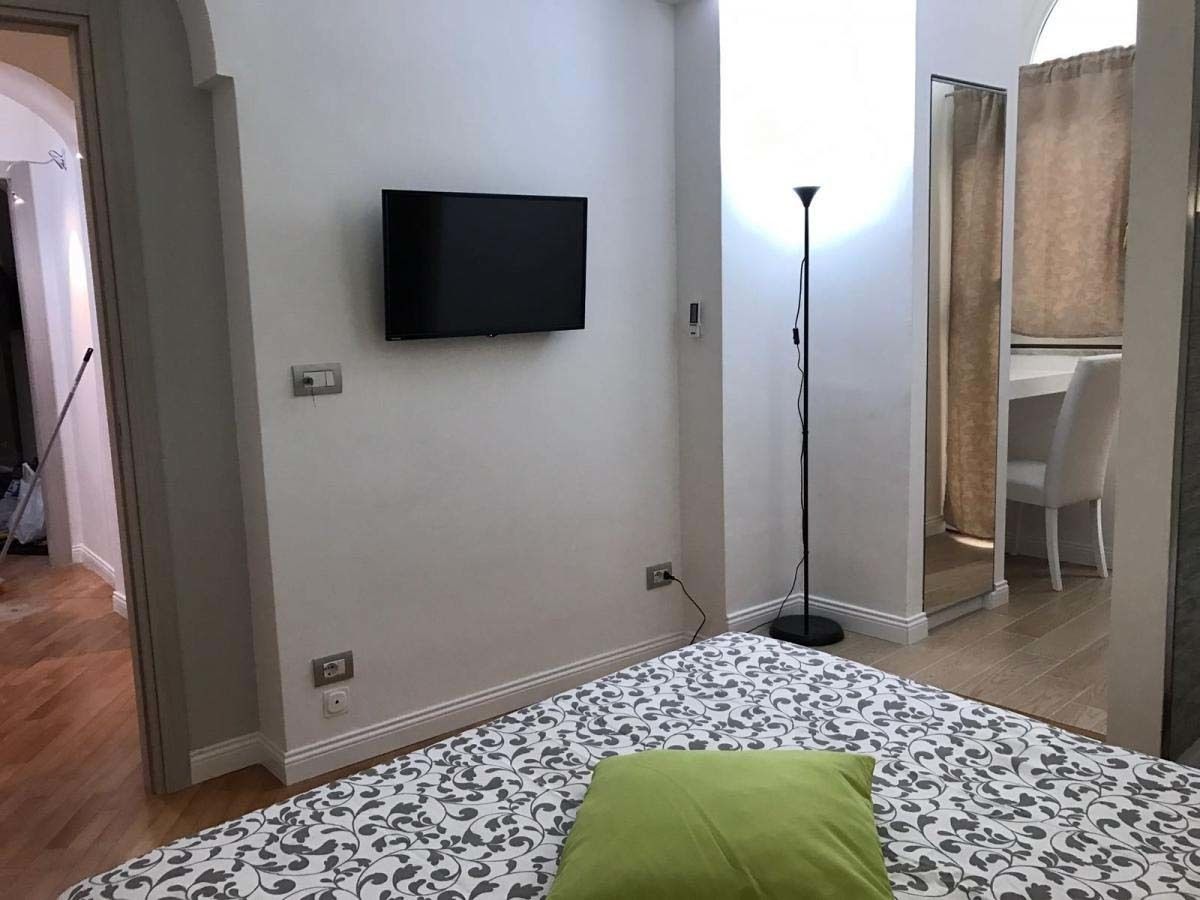 A bedroom with a bed, a TV mounted on the wall, and a desk with a chair in the corner.