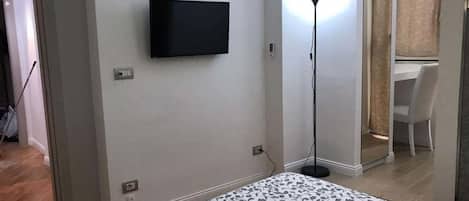 A bedroom with a bed, a TV mounted on the wall, and a desk with a chair in the corner.