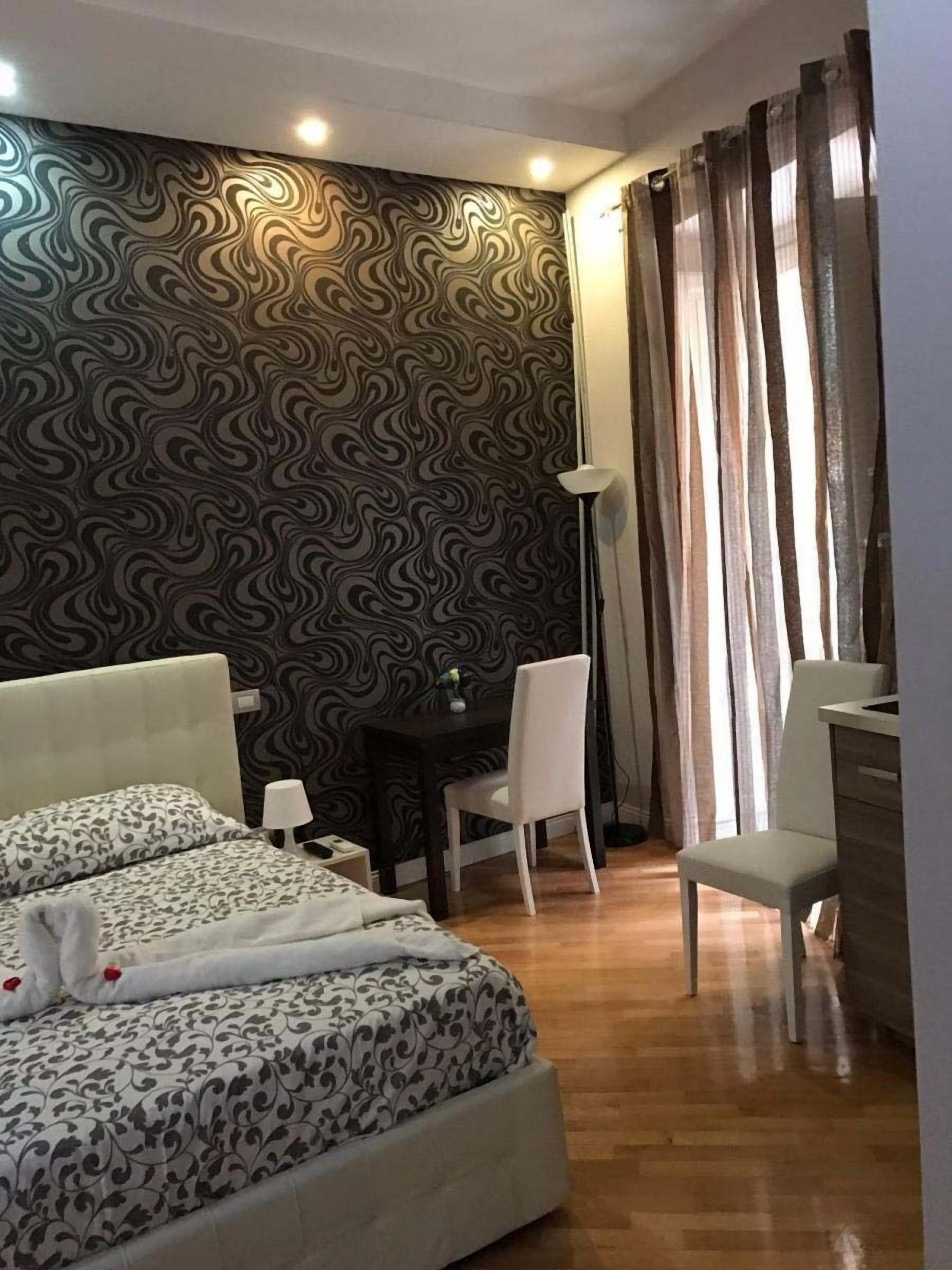 Ein Hotelzimmer mit gemustertem Wandteppich, einem Bett mit passendem Überwurf, einem Schreibtisch mit Stuhl und einer Lampe.