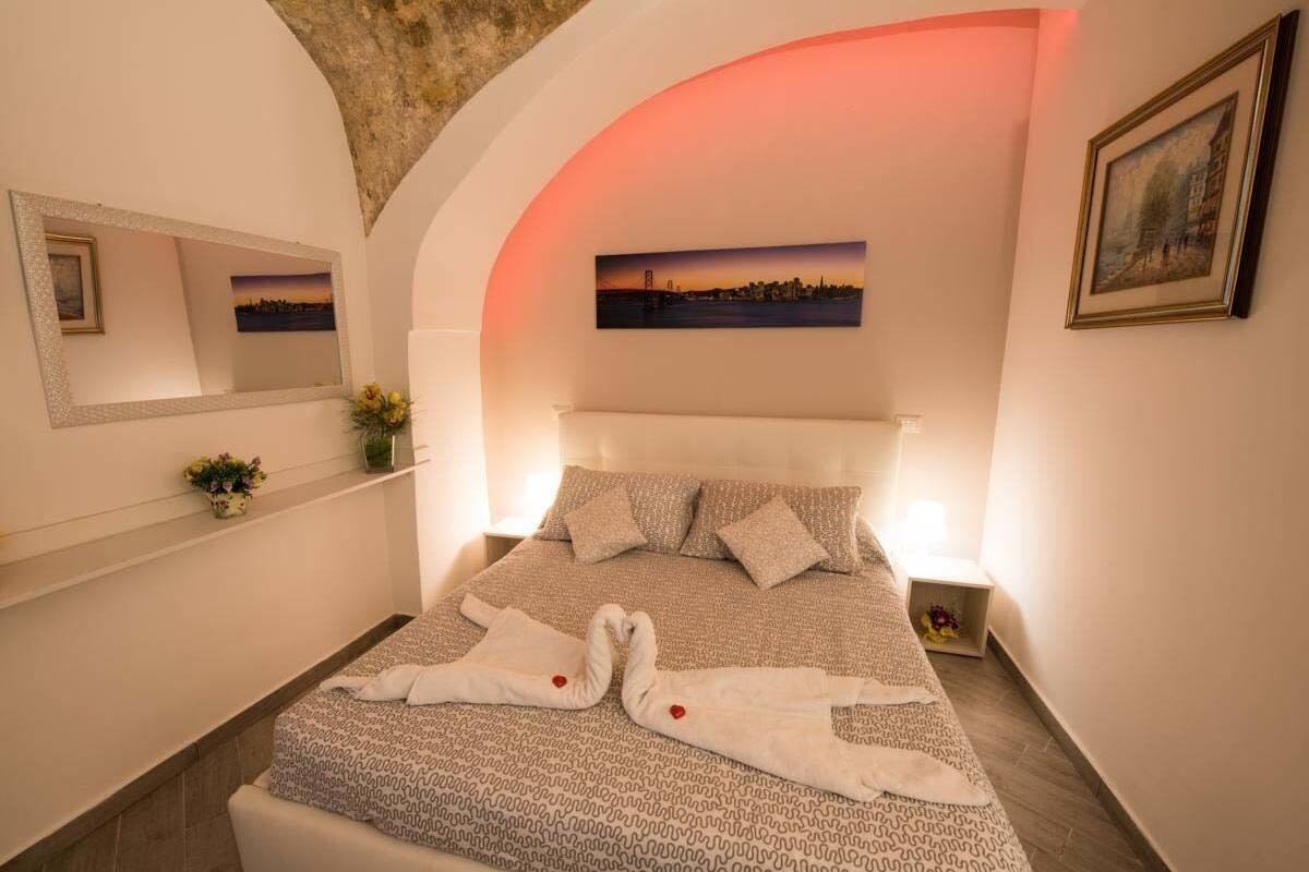 A neatly arranged bedroom with a bed, a bedside table, a nightstand, a mirror, and a picture on the wall.