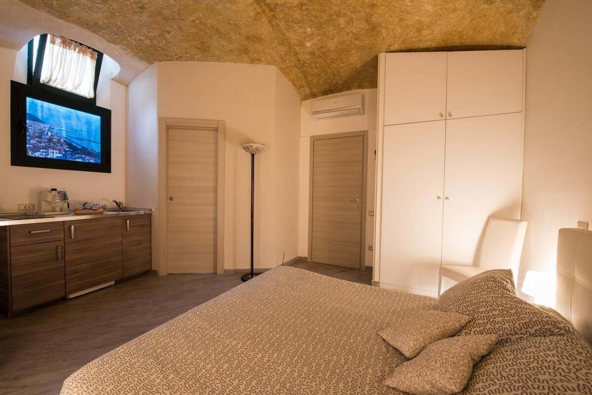 A bedroom with a bed, a wardrobe, a desk with a TV, and a floor lamp.