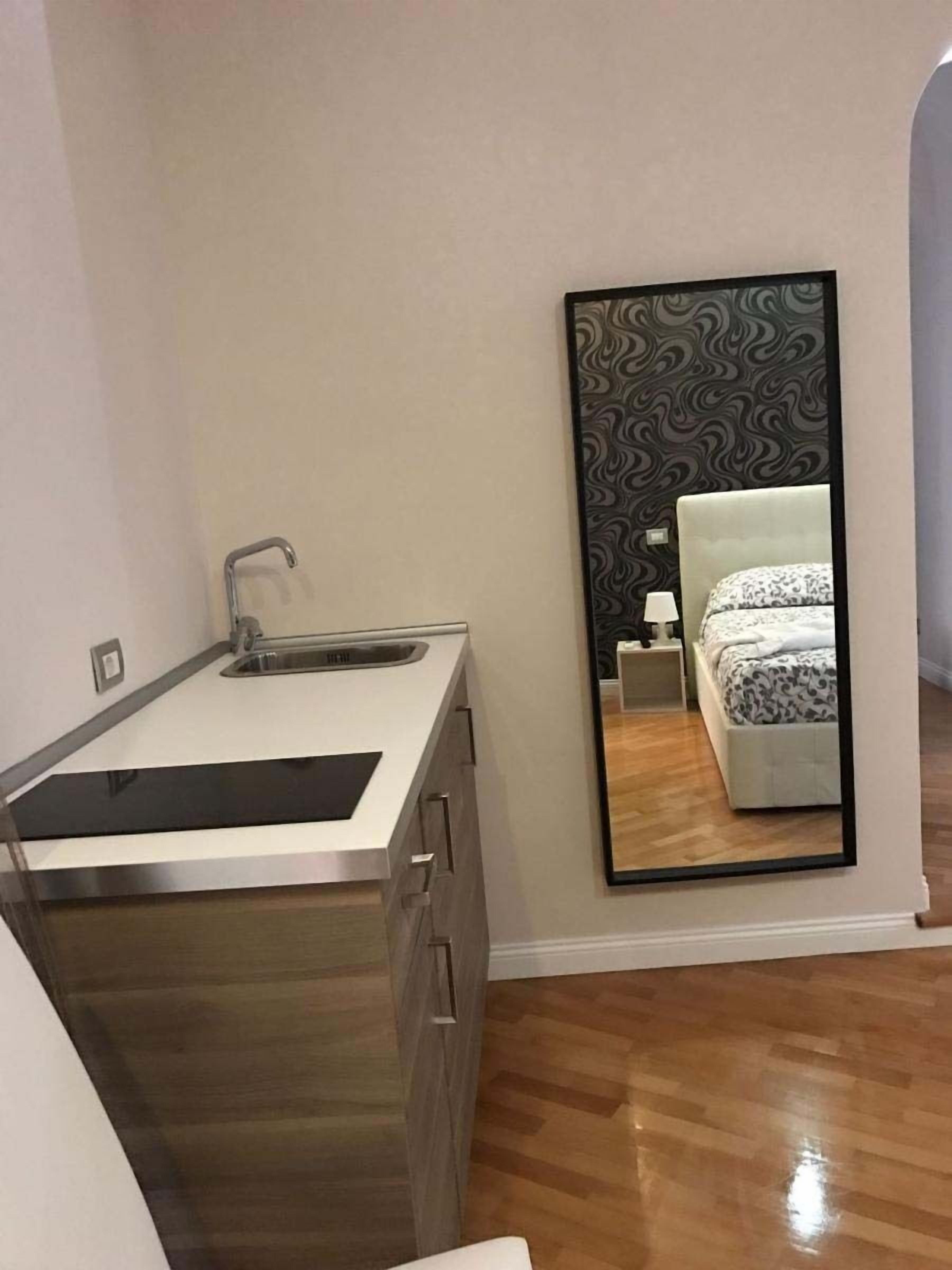 A modern bathroom with a sink, mirror, and a bed with a patterned bedspread.