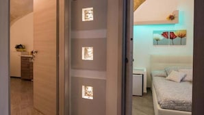 Un pasillo que conduce a un dormitorio con una cama, una mesita de noche y un estante en la pared con objetos decorativos.