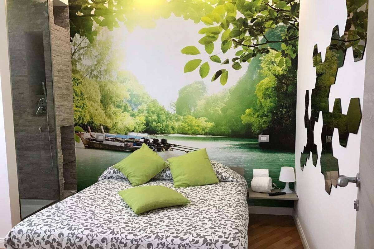 A bedroom with a bed, green pillows, a nightstand, and a mural of a river scene.