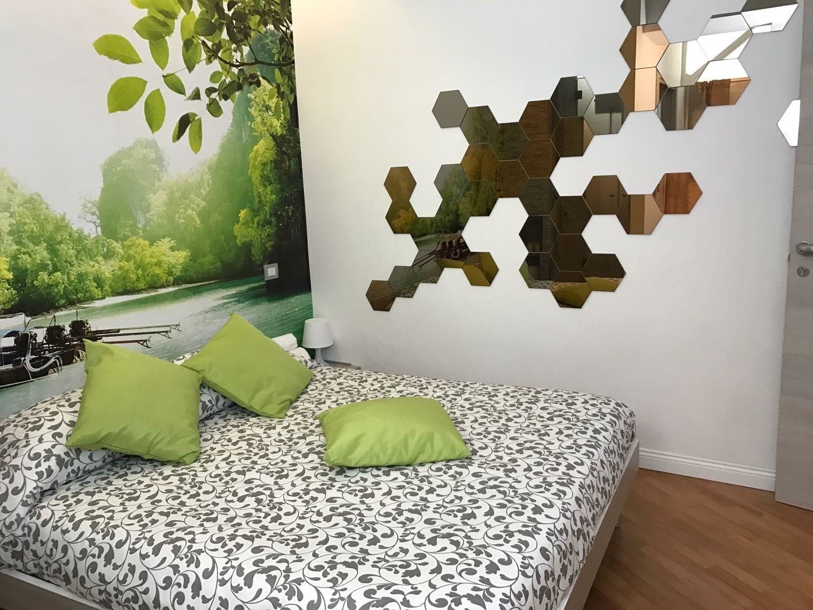 A bedroom with a bed, green pillows, a wall mural, and a hexagonal mirror.
