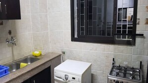 A compact kitchen with a washing machine, a gas stove, and a blue gas cylinder. - Résidence Olivier (Abidjan)