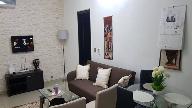 A living room with a brown sofa, a glass coffee table, and a TV mounted on the wall. - Résidence Olivier (Abidjan)