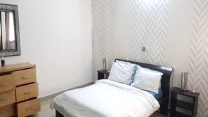 A bedroom with a bed, a dresser, a nightstand, and a mirror. - Résidence Olivier (Abidjan)