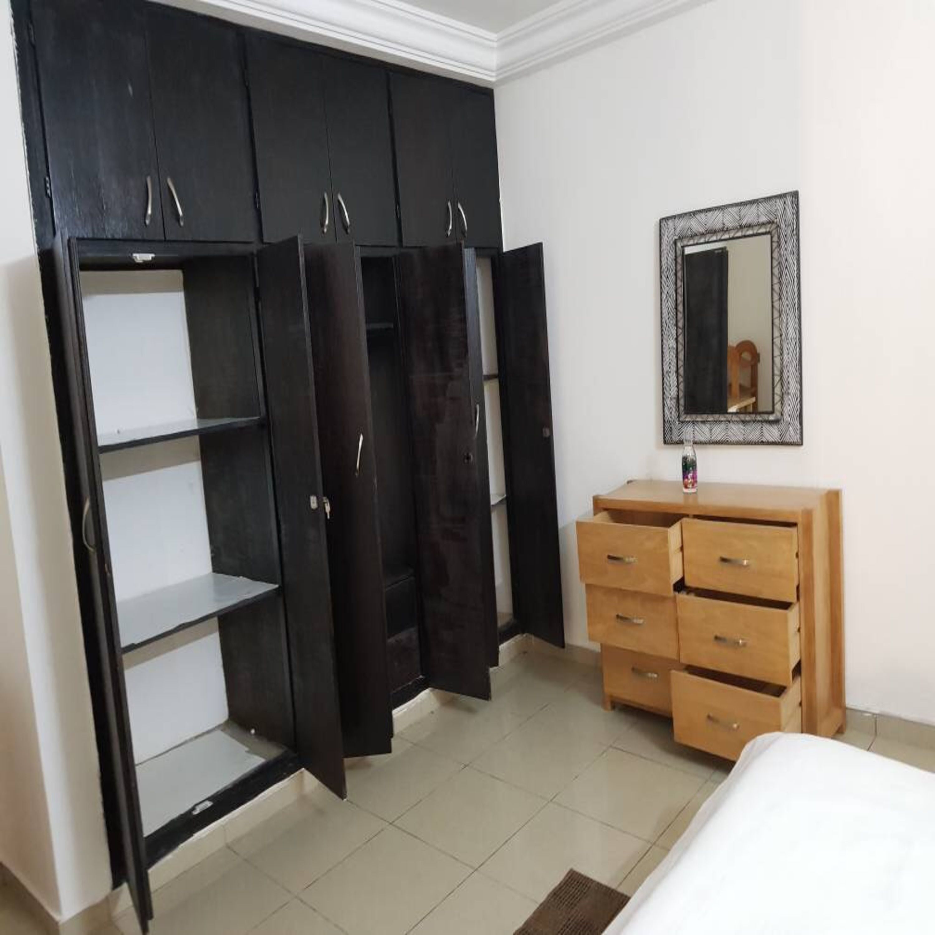 A bedroom with a black wardrobe, a wooden dresser, a mirror, and a bed.