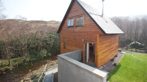 A wooden cabin with a sloped roof, a chimney, and a door leading to an interior space. - Inversnaid Bunkhouse - Hostel (Arrochar)