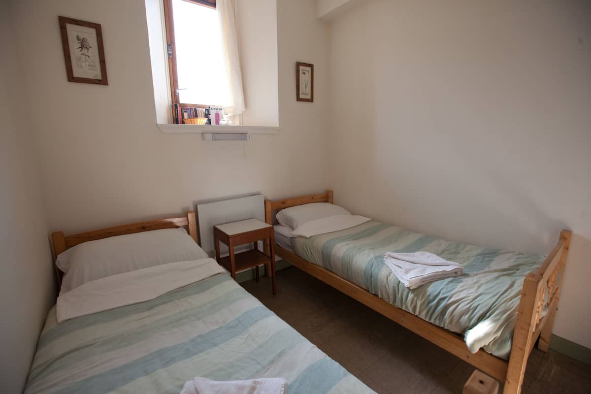 A bedroom with two single beds, a wooden nightstand, and a window with a curtain.