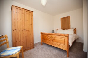 A bedroom with a wooden bed, a wooden wardrobe, and a chair with a checkered cushion.
