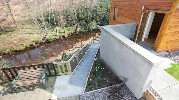 A wooden cabin with a concrete staircase leading to a deck overlooking a stream. - Inversnaid Bunkhouse - Hostel (Arrochar)
