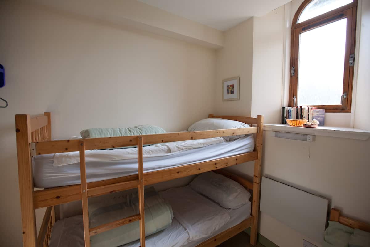 A bunk bed room with a window and a small shelf with books.