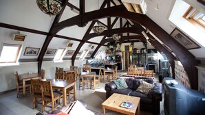 A spacious loft with high ceilings, exposed wooden beams, a dining area, a living room with a leather sofa, and a television. - Inversnaid Bunkhouse - Hostel (Arrochar)