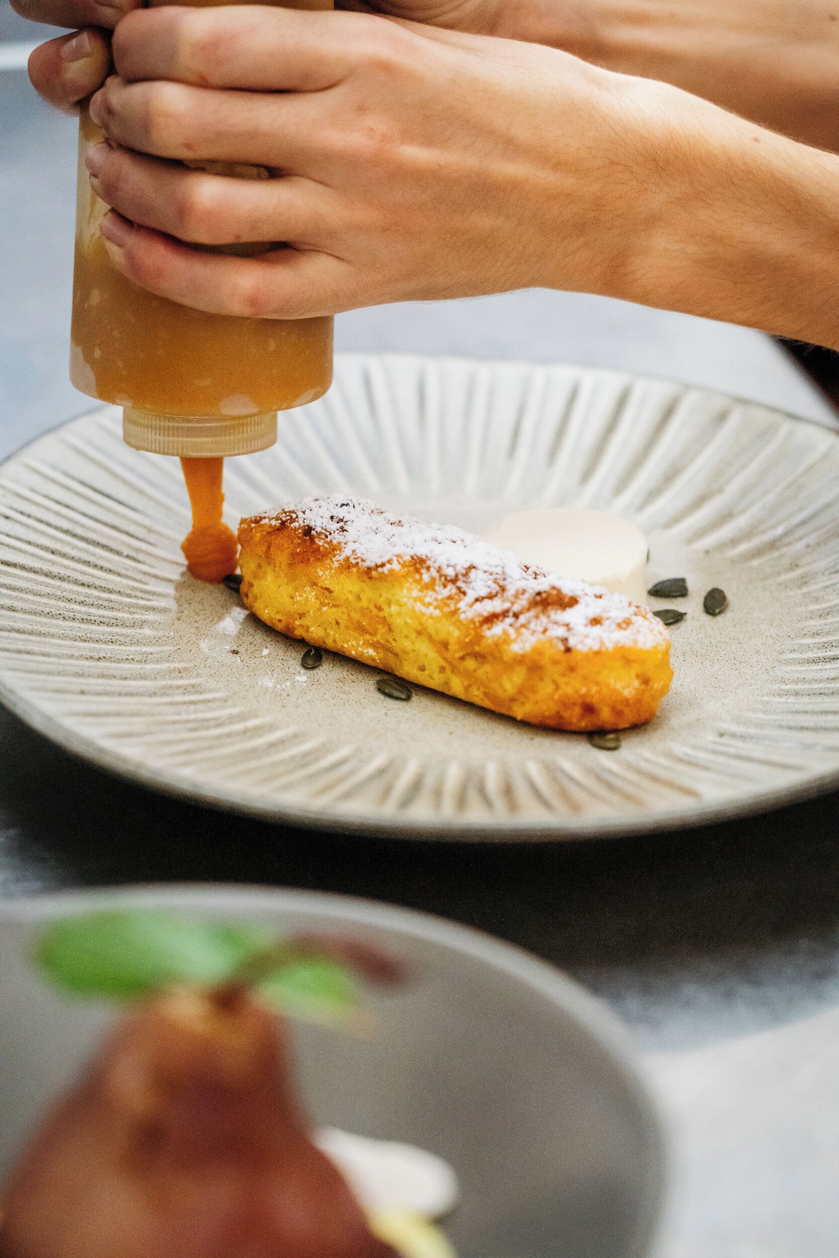 A person pouring a sauce onto a dessert on a plate.