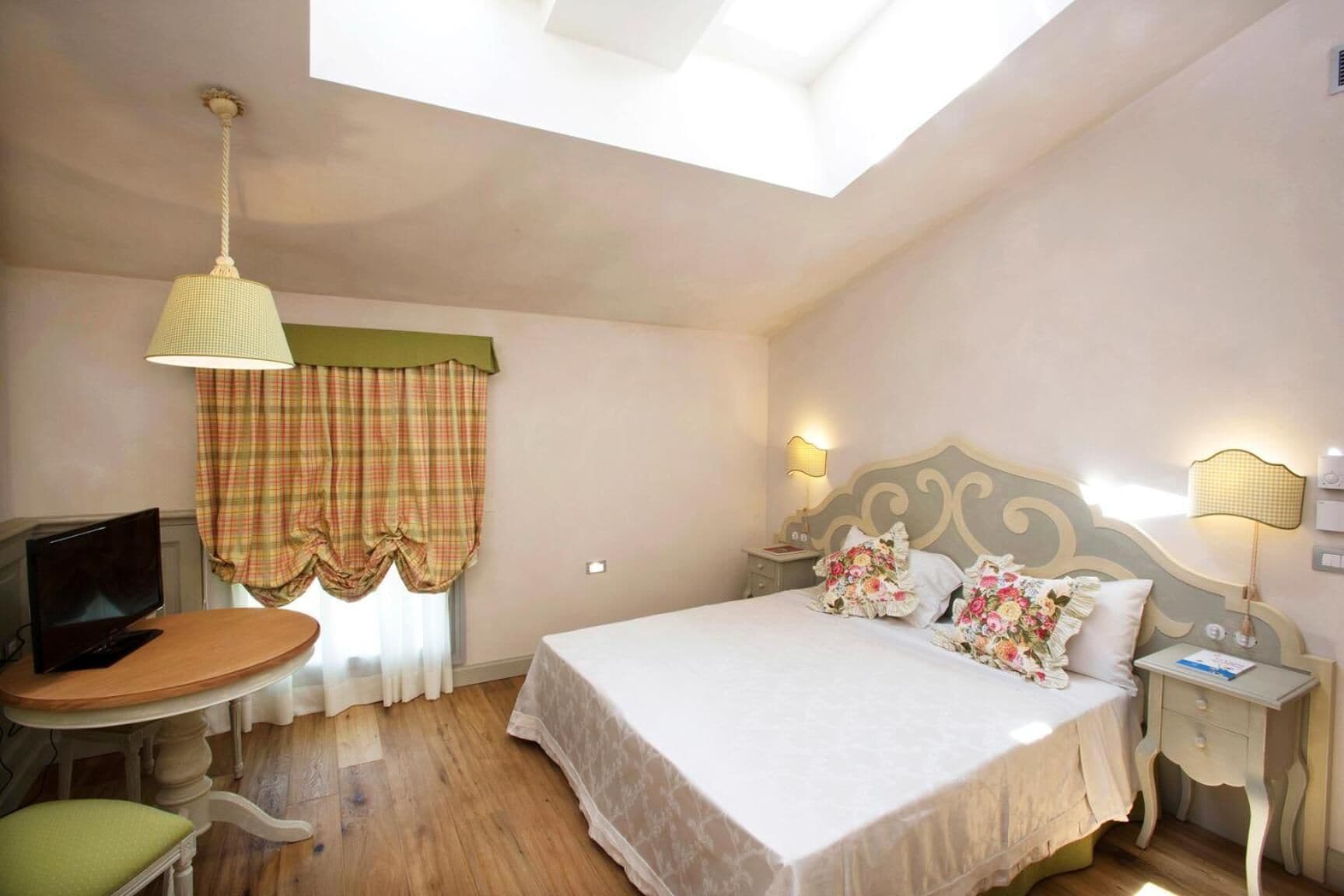 A bedroom with a bed, a desk, a television, and a window with curtains.