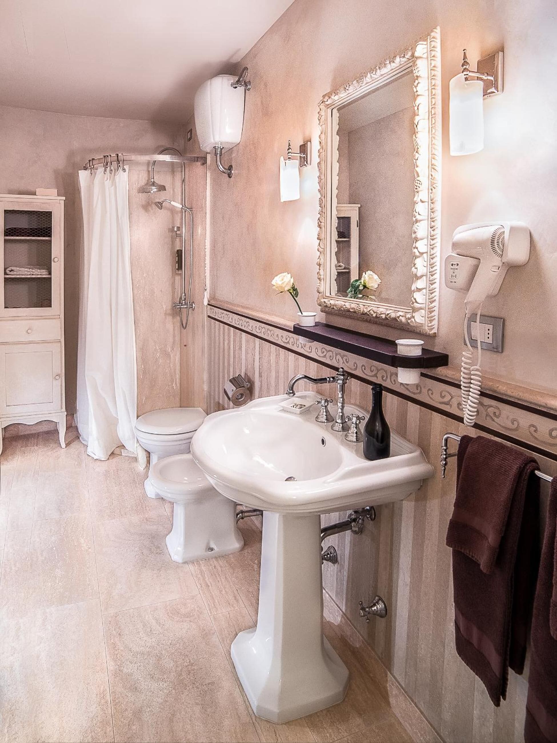 Ein Badezimmer mit einem weißen Standwaschbecken, einer Toilette, einer Dusche mit Glastür, einem Waschtisch mit Spiegel und einem an der Wand montierten Föhn.