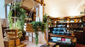 A bar area with wooden shelves stocked with bottles, a wooden counter with a bowl, and hanging plants. - Casa del Vino della Vallagarina (Isera)