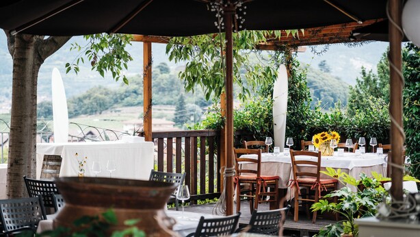 An outdoor dining area with tables set for two, surrounded by greenery and a view of the countryside. - Casa del Vino della Vallagarina (Isera)