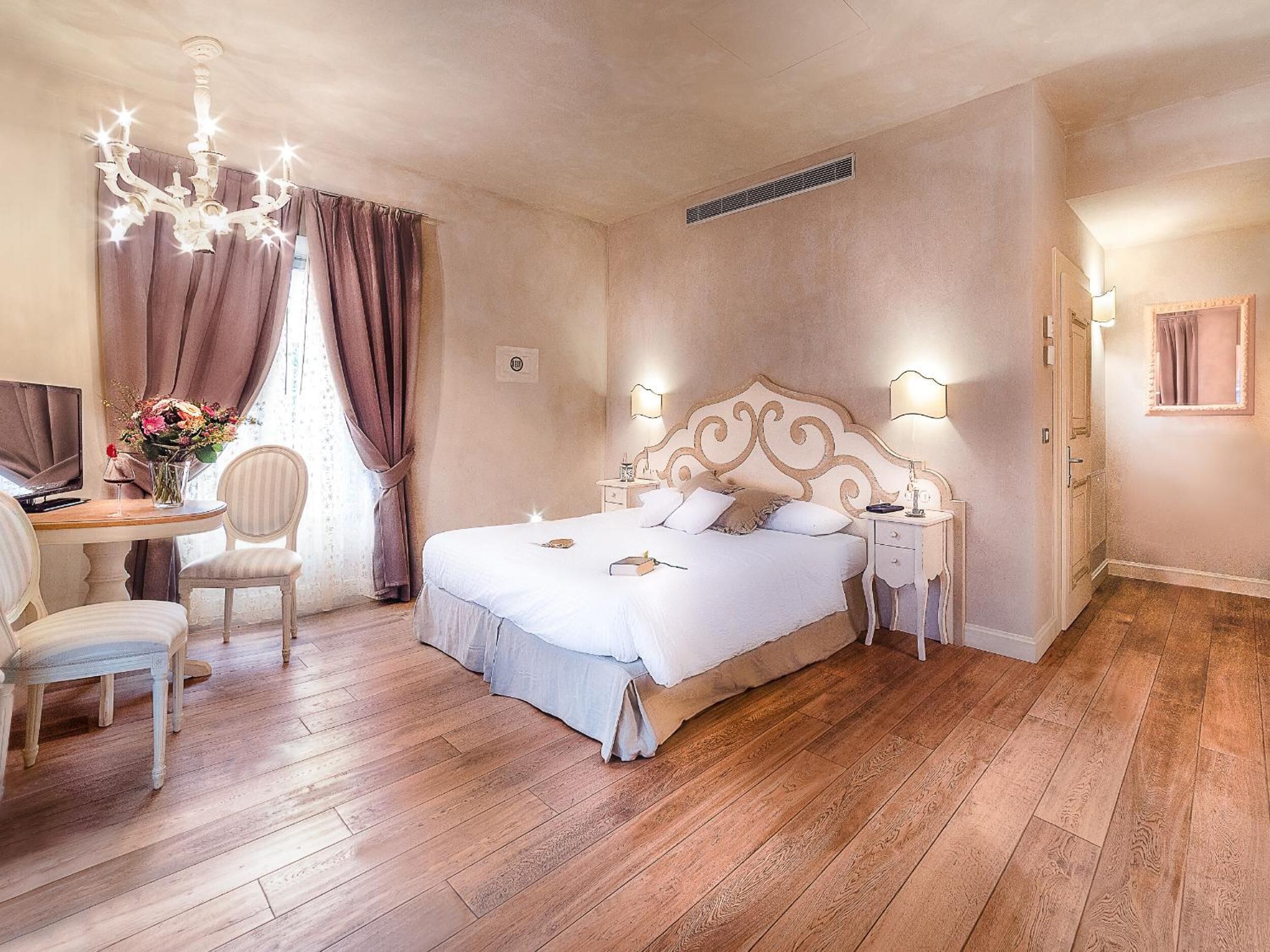 Ein Schlafzimmer mit einem großen Bett, einem Schreibtisch mit Stuhl, einer Deckenleuchte und einem Fenster mit Vorhängen.