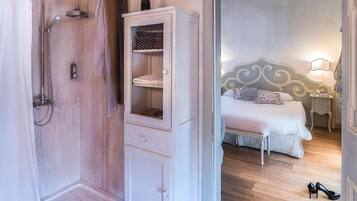Une chambre avec une douche, une armoire blanche, un lit avec une tête de lit et une table de chevet avec une lampe.