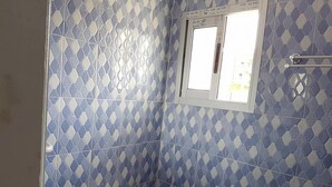 A bathroom with blue and white patterned tiles, a toilet, and a window with a view of the outside.