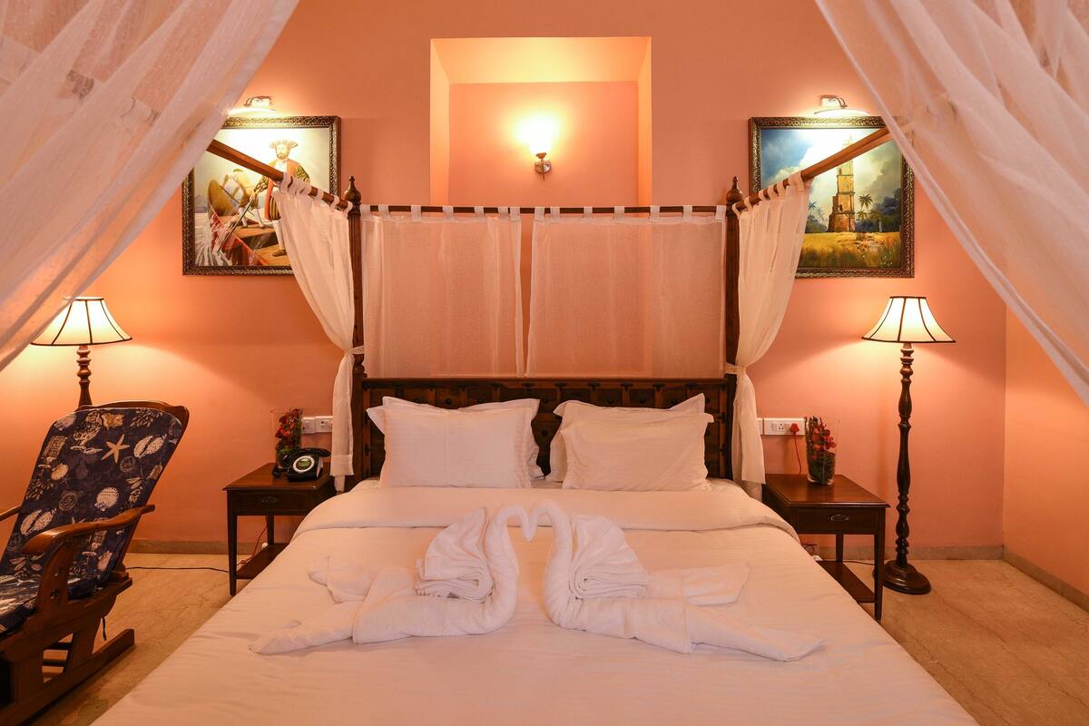 Une chambre d’hôtel avec un lit, deux lampes de chevet, une chaise et deux tableaux accrochés aux murs.