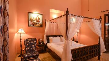 A four-poster bed with a canopy, a chair with a starfish pattern, a bedside table with a lamp, and a painting on the wall.