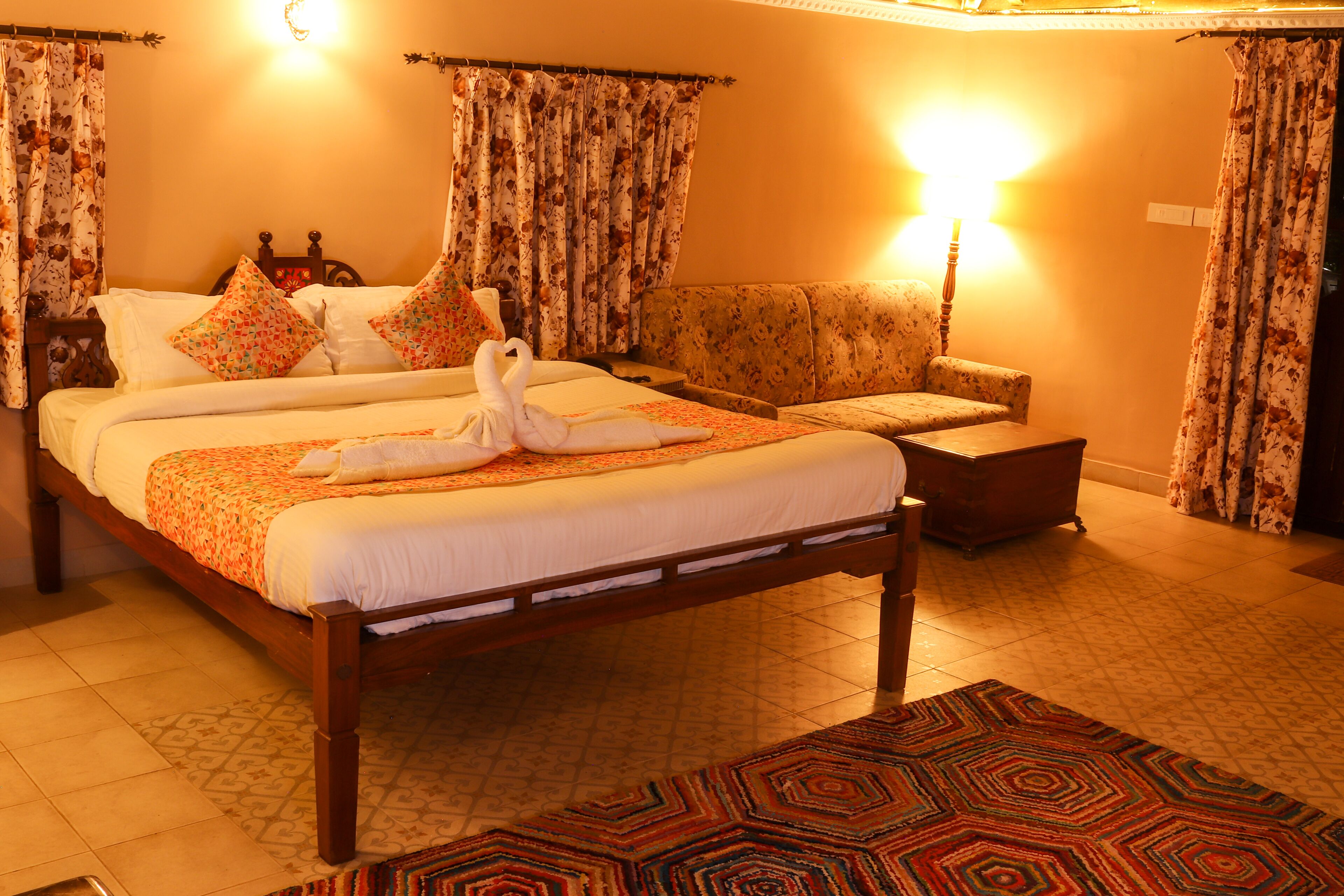 Habitación de hotel con una cama grande, un sofá, un tapete estampado y cortinas con motivos florales.