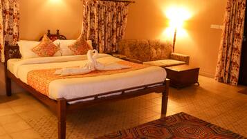 Habitación de hotel con una cama grande, un sofá, un tapete estampado y cortinas con motivos florales.