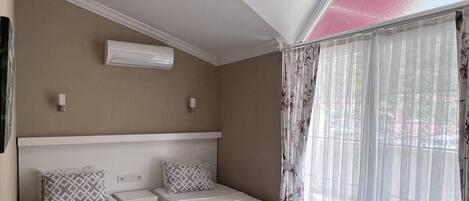 Ein Schlafzimmer mit zwei Betten, einer Bank, einem Deckenventilator und einem Fenster mit durchsichtigen Vorhängen.