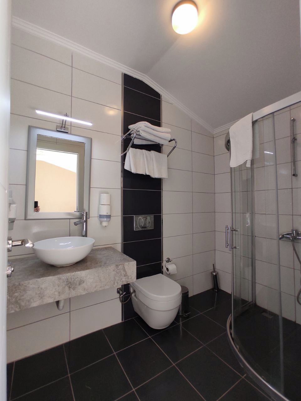 Ein modernes Badezimmer mit einem großen Spiegel, einem weißen Waschbecken, einer Toilette und einer Duschkabine.