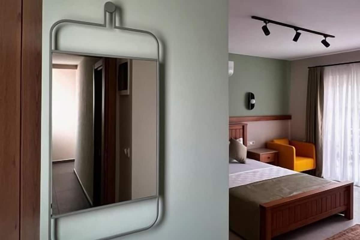 A bedroom with a bed, a bedside table, a chair, and a mirror on the wall.