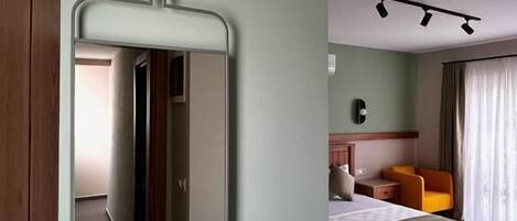 Un dormitorio con cama, mesita de noche, una silla y un espejo en la pared.
