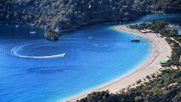 Una zona costera con una playa arenosa, mar azul cristalino y una pequeña isla con árboles.