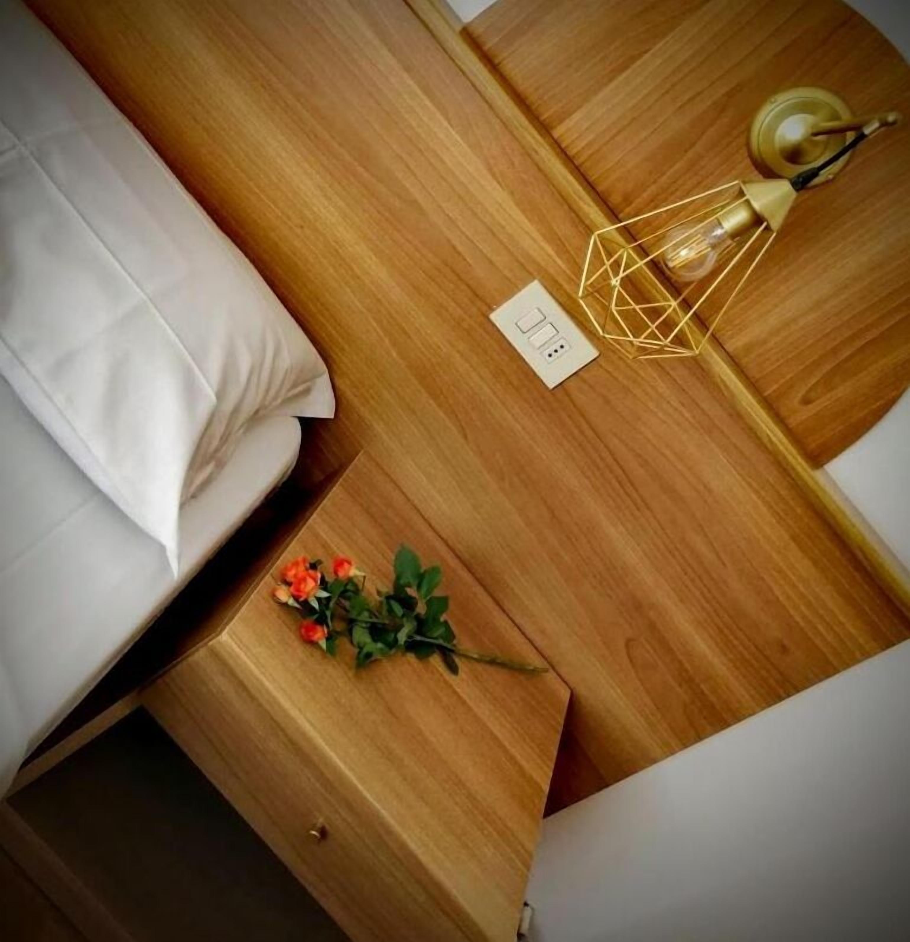 Un lit bien fait, avec du linge de lit blanc, une table de chevet avec une lampe et un petit bouquet de fleurs.