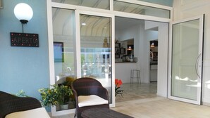 A modern living area with wicker furniture, a glass door leading to a kitchen, and a sign reading "APERTO". - Hotel Souvenir (Caorle)