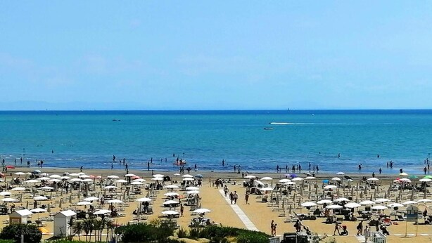 A beach with numerous umbrellas and sun loungers, a clear sky, and the ocean in the background. - Hotel Souvenir (Caorle)