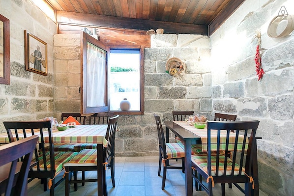 A rustic dining area with stone walls, wooden ceiling, and a window with an open door. - B&B La Casetta (Cavallino)