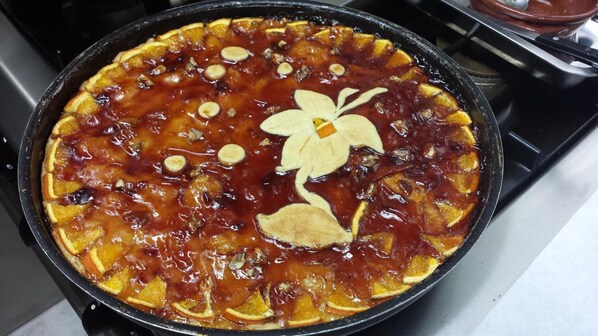 Un postre en una fuente, posiblemente una tarta o pastel, con rodajas de fruta y una flor decorativa hecha de masa.