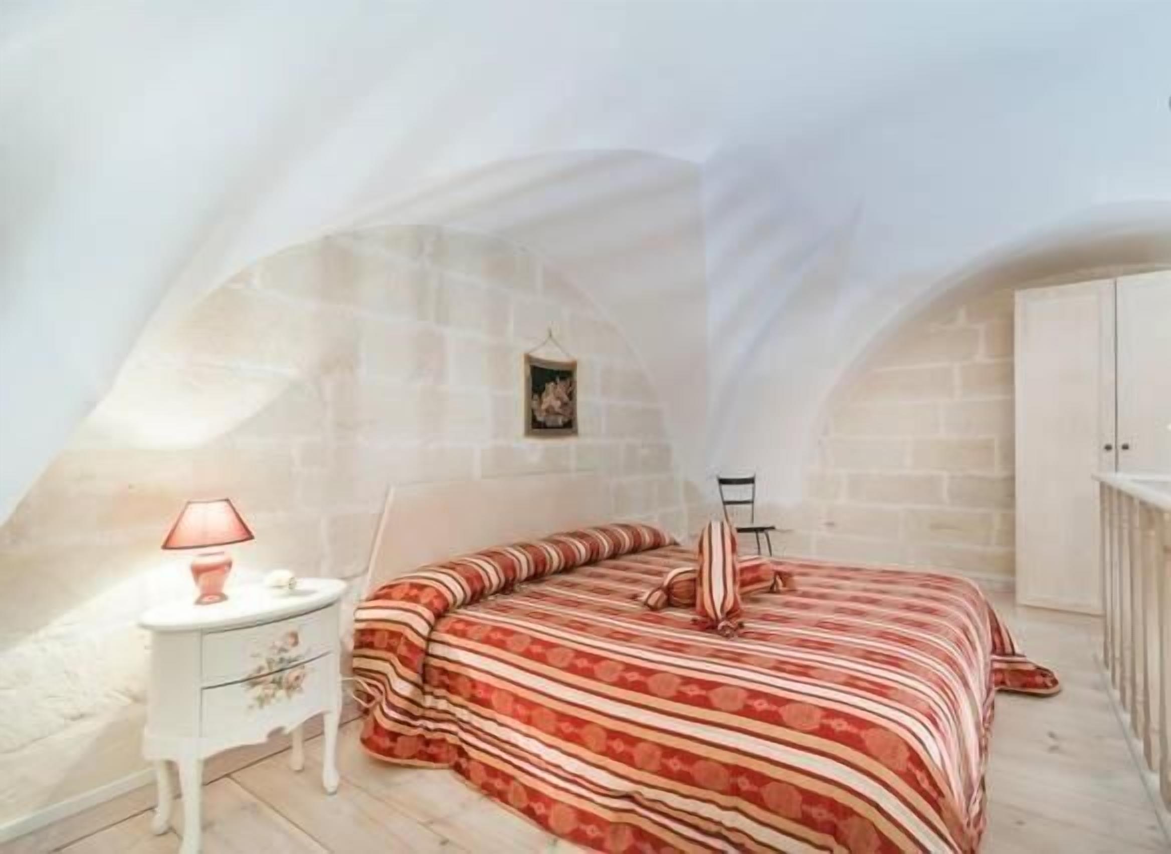 Ein Schlafzimmer mit schrägen Wänden, einem Bett mit gestreifter Bettwäsche, einem Nachttisch mit Lampe und einem kleinen Bild an der Wand.