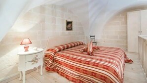 Un dormitorio con techo inclinado, una cama con ropa de cama a rayas, una mesita de noche con lámpara y un pequeño cuadro en la pared.