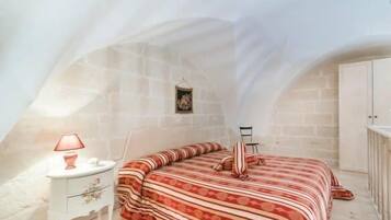 Ein Schlafzimmer mit schrägen Wänden, einem Bett mit gestreifter Bettwäsche, einem Nachttisch mit Lampe und einem kleinen Bild an der Wand.