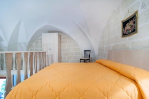 Un dormitorio con una cama grande, techo abovedado, una silla e imagen enmarcada en la pared.