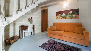 Una sala de estar con una escalera, un sofá, un cuadro, una mesa de comedor y una silla.